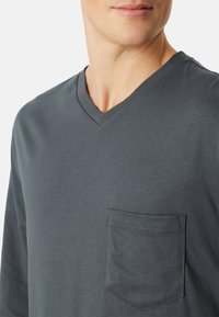 Graues V-Ausschnitt Langarmshirt aus weichem, leichtem Stoff. Verfügt über eine Brusttasche mit ordentlich genähten Details.