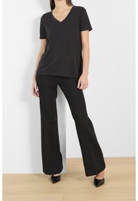 Svart t-shirt med V-hals i mjukt tyg, kombinerad med svarta vida byxor. Strapiga svarta klackskor fulländar outfiten. Minimalistisk design.