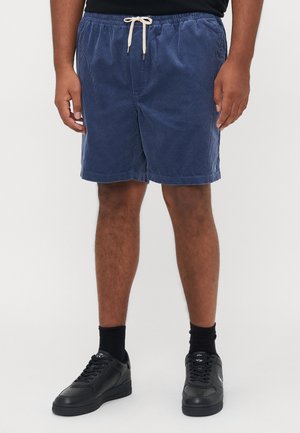 Navy corduroy shorts with an elastic waistband and drawstring, featuring side pockets and a relaxed fit; worn with black sneakers and socks.