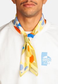 Homme portant une chemise blanche avec le logo "Dilly" bleu et une écharpe colorée aux motifs abstraits bleus, jaunes, oranges et verts nouée autour du cou.