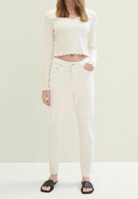 Vitt ribbat långärmat topp med vågig nederkant, kombinerat med vita högmidjade jeans med fransad nederkant, och svarta slidessandaler.