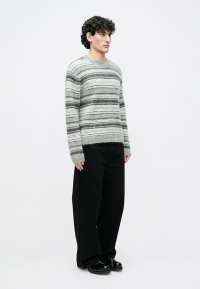 Prugasti džemper u svijetlosivoj i tamnosivoj boji, izrađen od mekanog materijala, s okruglim izrezom i rebrastim manšetama, uparen s širokim crnim hlačama.