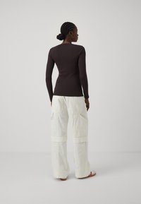 Haut à manches longues de couleur marron foncé associé à un pantalon cargo ample de couleur crème avec des poches et un ourlet retroussé. Des sandales neutres complètent le look.