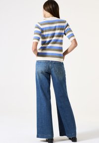 Korte mouwen gestreepte trui in roomkleur, blauw en olijfgroen; gecombineerd met wijdgevallen blauwe denim jeans, met achterzakken en een relaxte pasvorm.