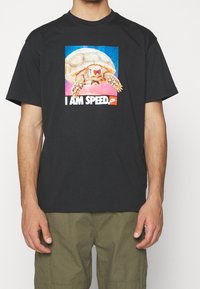 Camiseta de algodón negra con un gráfico colorido de una tortuga y el texto "SOY VELOZ" en letras blancas en negrita en el centro.