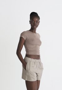 Brown fitted short-sleeve top paired with light beige high-waisted shorts, made from soft fabric with an elastic waistband and side pockets.