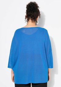 Blusa blu, trasparente, oversize con maniche a tre quarti e orlo leggermente curvo. Tessuto morbido, leggero e un design semplice.