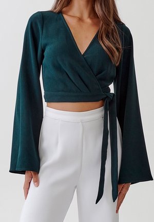 Groen wikkelshirt met lange mouwen en een diepe V-hals, gemaakt van een zachte stof, met een gestrikt tailleband en bijpassende witte, hooggetailleerde broek.