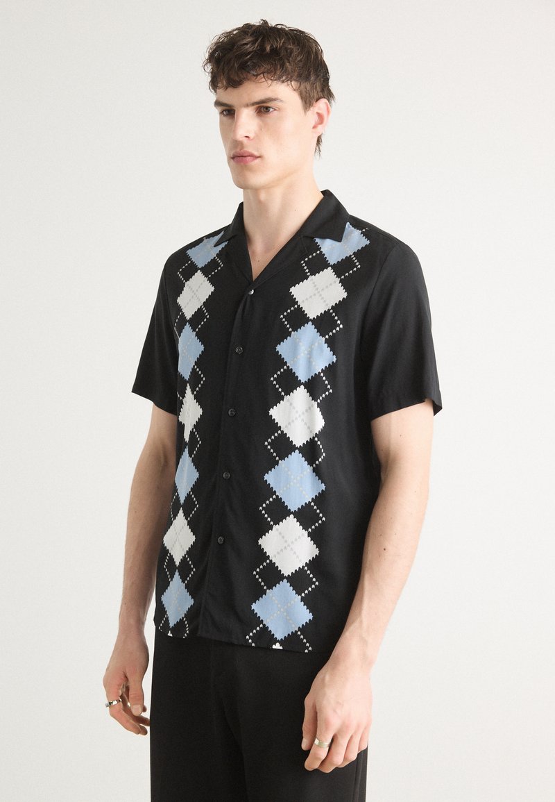 Chemise noire à manches courtes avec un motif de losanges bleu et blanc, dotée d'une texture lisse et d'un design à boutons sur le devant.