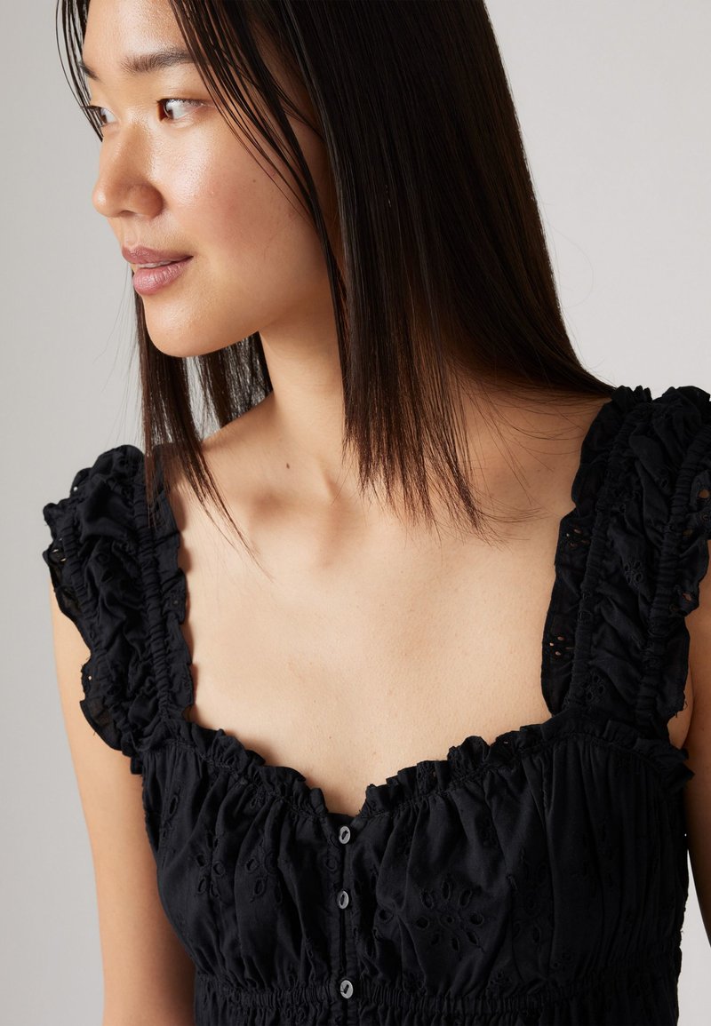 Vestido negro con mangas rizadas, escote cuadrado, textura bordada con flores y detalles de botones en la parte delantera. Tejido suave y ligero.