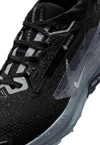 Zapatillas Nike Pegasus Trail 5 GT negras con Gore-Tex, que cuentan con un upper texturizado, gotas de agua y una entresuela gris que proporciona agarre y soporte.
