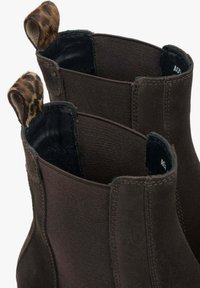 Brązowe zamszowe botki za kostkę z elastycznymi panelami bocznymi i uchwytami w leopardzi wzór, charakteryzujące się usztywnioną konstrukcją i teksturowanymi powierzchniami.