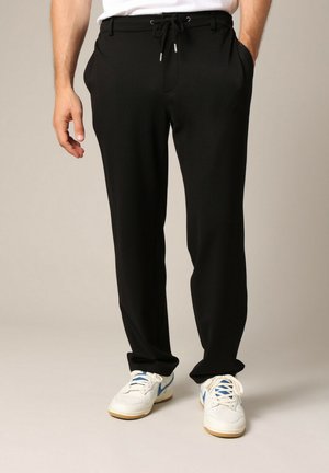 Zwarte broek van zachte stof, met een elastische tailleband, een relaxte pasvorm en zijzakken; gecombineerd met witte sneakers met blauwe accenten.