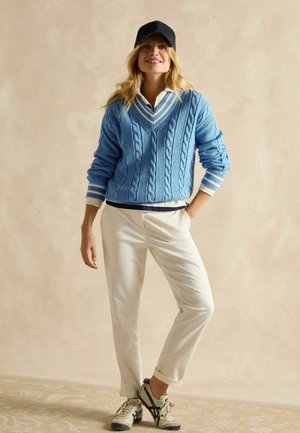 Light blue cable-knit sweater with white trim and V-neck, paired with white chinos and gray sneakers. The cap is navy blue.