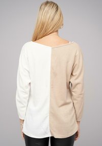 Langsleeve top met een splitontwerp; de ene kant is wit, de andere beige. Heeft een brede halslijn en een zachte, gestructureerde stof.
