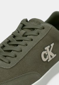 Αθλητικό παπούτσι από πράσινο σουέντ με υφασμάτινα κορδόνια στο ίδιο χρώμα, λευκή σόλα και αντίθετο λογότυπο "cK" στο πλάι.