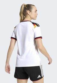 White sports jersey with short sleeves, black, red, and yellow accents on shoulders and sleeves, paired with black shorts featuring white stripes.