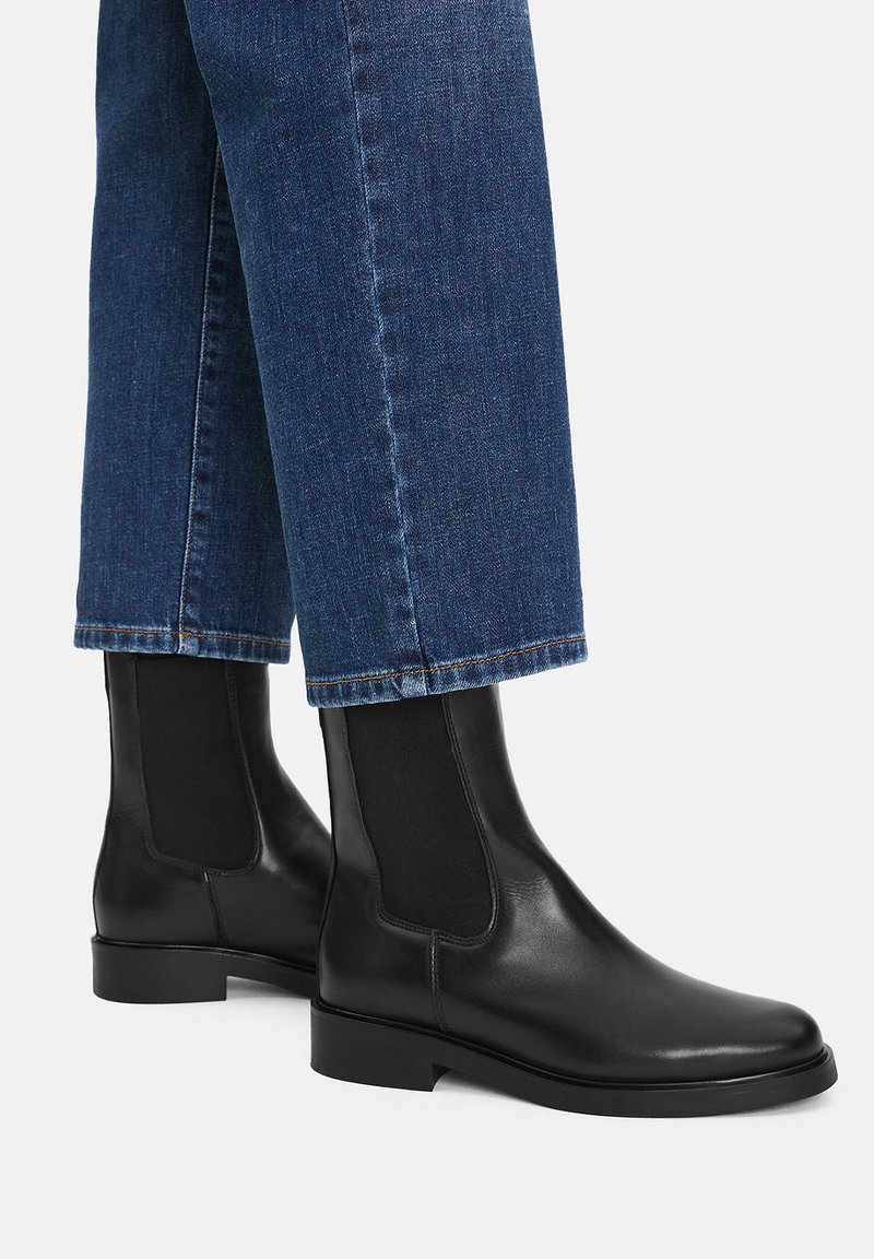 Mustad nahast pahkluu saapad elastsete külgpaneelidega ja sileda tekstuuriga, koos siniste sirgete säärtega teksadega, millel on toores serv.