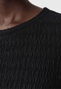 Zwarte, gestructureerde top met een gewelfde patroon, ronde halslijn en een zachte stofafwerking, die een golvend oppervlakontwerp benadrukt.
