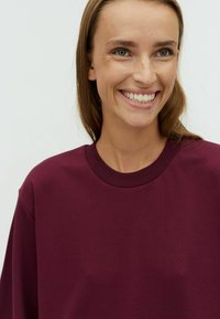 Burgundy sweatshirt with a crew neckline, smooth texture, and dropped shoulders; features a relaxed fit and minimalistic design details.