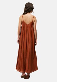 Luftiges Maxikleid in Rostfarbe, aus leichtem Stoff gefertigt. Verfügt über Spaghettiträger und einen gerafften Rücken, der eine entspannte Silhouette bietet.