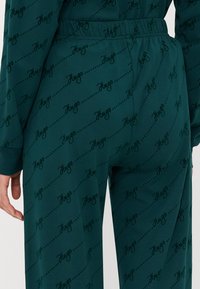 Vihreät pyjamahousut, joissa on pehmeä rakenne, ja joissa on toistuva musta "Hugo" -kuvio sekä mukava joustava vyötärö.