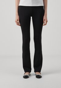 Črne slim-fit hlače z gladko teksturo in subtilnimi sprednjimi šivi, v kombinaciji s črnimi in srebrnimi balerinkami, na nevtralni ozadju.