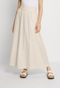 Jupe maxi beige avec taille élastique, dotée d'un léger motif texturé. Associée à des sandales simples à deux brides.