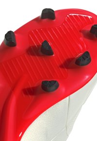 Suela moldeada roja con costillas elevadas y tachuelas negras. Parte superior blanca con acabado texturizado, que presenta una costura prominente a lo largo del costado.