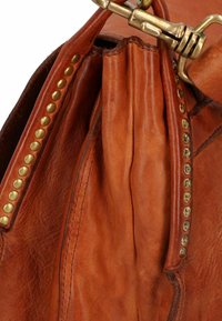 Borsa a mano in pelle marrone con borchie in ottone lungo la cucitura, che presenta una superficie testurizzata e dettagli plissettati vicino all'apertura.