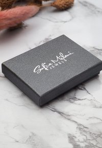 Grå rektangulær smykkeboks med struktureret overflade, der har prægede hvide bogstaver "Sofia Milani Jewels" på låget.