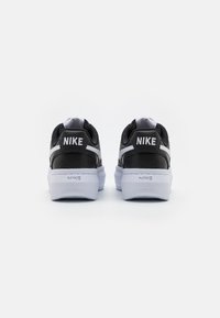 Svarta Nike-sneakers med vita detaljer, med en texturerad ovandel, vadderad krage och en tjock vit sula. Logga på hälen och sidan.