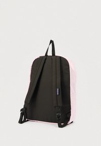 Vue arrière d'un sac à dos rose et noir avec des bretelles rembourrées réglables et une boucle de suspension sur un fond uni.