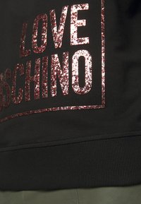 Černá mikina s velkým, třpytivým nápisem "LOVE" a "MOSCHINO" ve růžové barvě. Nápis je orámován elegantním lemem pod spodním okrajem.