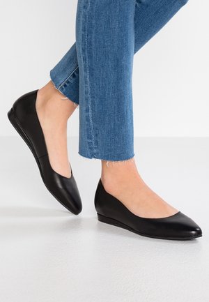 Ballerines en cuir noir avec bout arrondi et petit talon compensé, associées à un jean bleu coupé à la cheville avec ourlets effilochés.