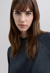 Donkergrijze trui met ronde hals en raglanmouwen, met een subtiel contrasterende stikdetail langs de naden.