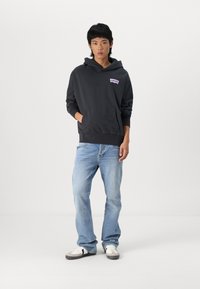 Sudadera con capucha negra con un bolsillo delantero y un logo blanco de Levi's. Llevada con jeans de mezclilla azul claros y zapatillas negras y blancas.