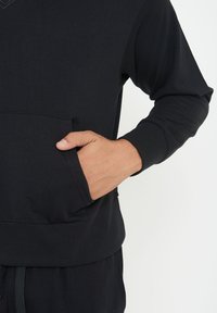 Black long-sleeve hoodie made of soft fabric, featuring a front pocket, ribbed cuffs, and a comfortable fit. Accents include subtle stitching.