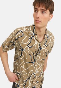 Chemise à manches courtes en tissu beige clair avec des motifs abstraits blancs et bleu marine. Conception à boutons avec une coupe décontractée.