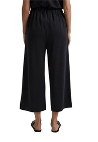 Culottes larges noires avec une coupe décontractée, dotées d'une taille élastique et d'une texture lisse, arrivant à mi-mollet.