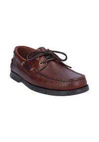 Zapato de barco de cuero marrón con punta redondeada, costuras blancas y diseño de cordones con ojales dorados y suela de goma texturizada.