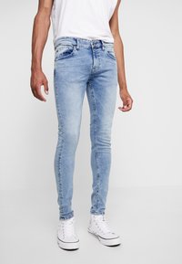 Ljusblå denim skinny jeans med en blekt finish, utrustade med fem fickor, bälteshällor och en tajt passform, som är kombinerade med vita canvas skor.
