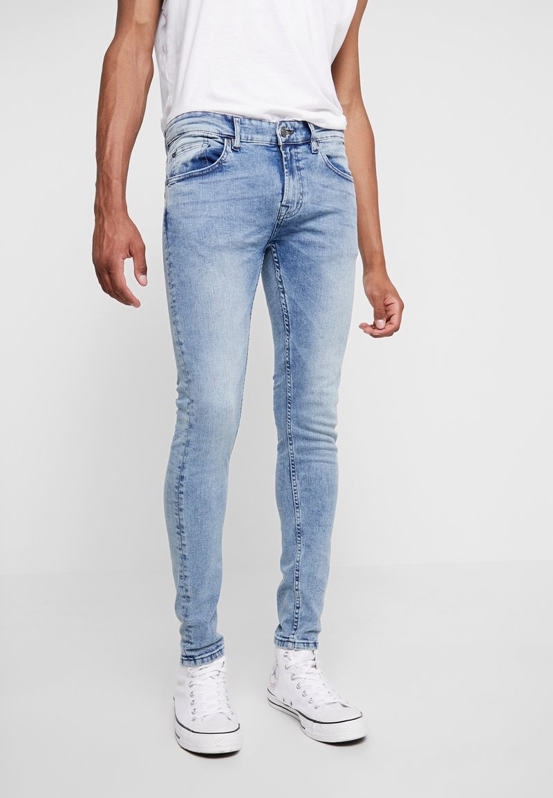 Ljusblå denim skinny jeans med en blekt finish, utrustade med fem fickor, bälteshällor och en tajt passform, som är kombinerade med vita canvas skor.
