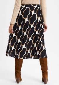 Faltenrock in Schwarz, Weiß und braunem Wellenmuster. Verfügt über einen Bund und fällt bis zur Mitte der Wade, kombiniert mit braunen Wildleder-Stiefeln über dem Knie.