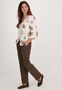 Witte blouse met bruin paisleyprint, driekwart mouwen; olijfgroene rechte broek; zwarte flats met gouden studs.