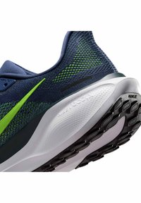 Dettaglio del tallone di una scarpa da corsa Nike blu navy e verde, con suola Nike React bianca testurizzata e battistrada nero.