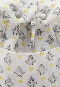 Mönstrad väska i vitt tyg med blommotiv i grått och gult. Inkluderar tryckknapp och dragkedjedetalj.