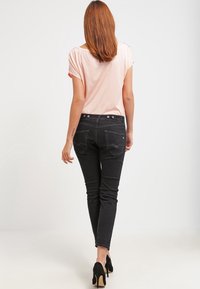 Svarta skinny jeans med bakfickor och dekorativt sömnad, parat med en ljusrosa topp med korta ärmar. Slät textur, avslappnad passform.