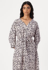 Long-sleeve dress in a light fabric with a black and white abstract pattern, v-neckline, and a waist tie detail.