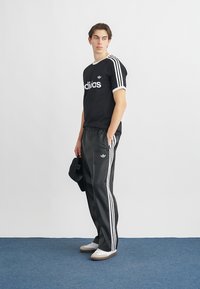 Czarny bawełniany t-shirt z białym logo "adidas" i trzema białymi paskami na ramionach, w zestawie z czarnymi spodniami dresowymi z bocznymi paskami.